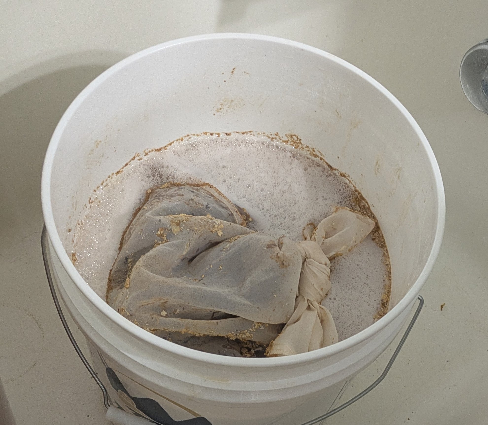 Photo of a mesh bag containing grape must floating on the surface of a meda fermentting in a bucket fermenter